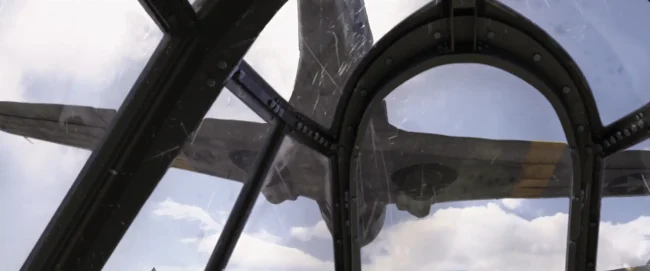 Film still looking up through a scratched cockpit canopy at a WWII fighter plane passing overhead against cloudy sky