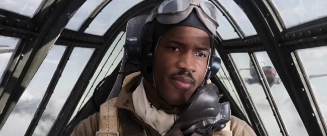 Film still of a WWII fighter pilot holding an oxygen mask, another aircraft visible through the cockpit glass behind