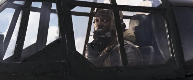 Film still of a WWII pilot wearing an oxygen mask looking out from behind the ribbed glass canopy of his fighter